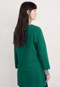 Groene longsleeve top met een relaxte pasvorm, middellange ontwerp en ribbelhalslijn, gelaagd over een gestreepte longsleeve shirt.
