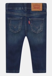 Jeans de denim azul con una textura suave, que presentan un diseño clásico de cinco bolsillos, bolsillos traseros bordados y una etiqueta de marca de cuero.