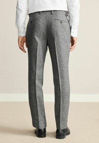 Gray wool trousers with a textured finish, flat front, and two back pockets, worn with black shoes. Tailored fit and straight leg design.