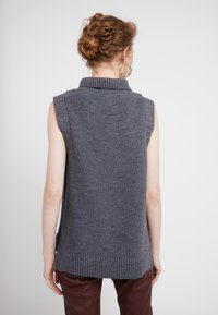 Gilet senza maniche grigio in maglia con collo e orlo a costine. Tessuto strutturato, spacchi laterali per facilità di movimento, mostrato da dietro.