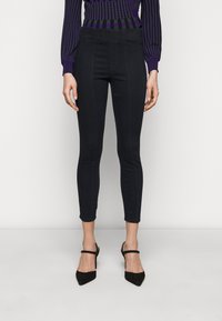 Černé skinny džíny s středním pasem, elastickým pasem a předními švy. V kombinaci s černými lodičkami s špičatou špičkou.