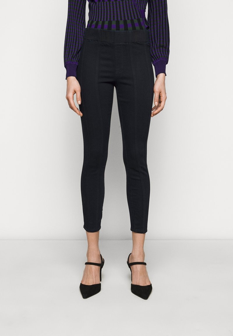 Černé skinny džíny s středním pasem, elastickým pasem a předními švy. V kombinaci s černými lodičkami s špičatou špičkou.