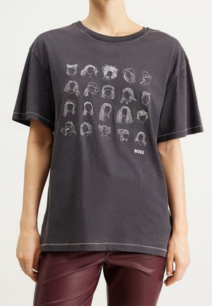 Camiseta negra de gran tamaño con 20 dibujos de líneas blancas de rostros abstractos y el texto "BOSS", combinada con pantalones de cuero rojo oscuro.