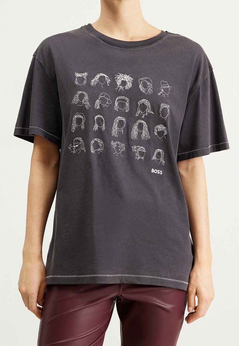 Svart oversized t-shirt med 20 vita abstrakta ansiktslinjeteckningar och texten "BOSS", bärs med mörkröda läderbyxor.