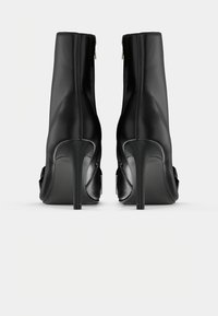 Zwarte leren enkelboots met een strak ontwerp, hoge stilettohakken en een ritssluiting aan de achterkant. Glide textuur, minimalistische stijl.
