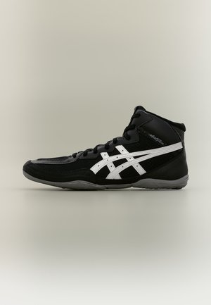 Chaussure de lutte montante noir et blanc avec des lacets et le logo de la marque sur le côté, sur un fond neutre uni.