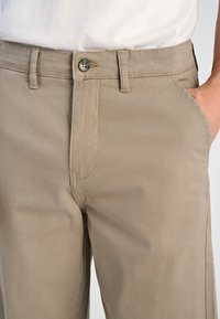 Tan katoenen broeken met een recht model, voorzien van een knoopsluiting aan de voorkant, zijzakken en zichtbare stikseldetails.