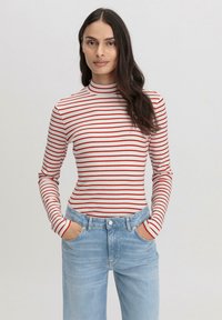 Gestreiftes rotes und weißes Rollkragenoberteil mit langen Ärmeln, kombiniert mit hellblauen Jeans. Der Stoff wirkt weich und hat eine figurbetonte Passform.