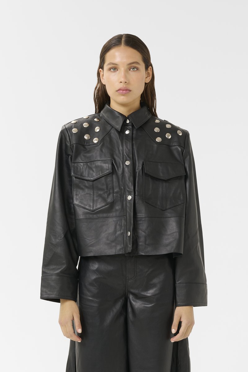 Zwarte leren cropped jack met twee voorzakken, knoopsluiting en zilverkleurige studs op de schouders. Gladde textuur.
