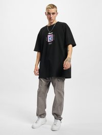 Sort oversized t-shirt med grafisk print i midten; sat sammen med lysegrå cargo-bukser og hvide sneakers. Sølv-halskæde detaljer.