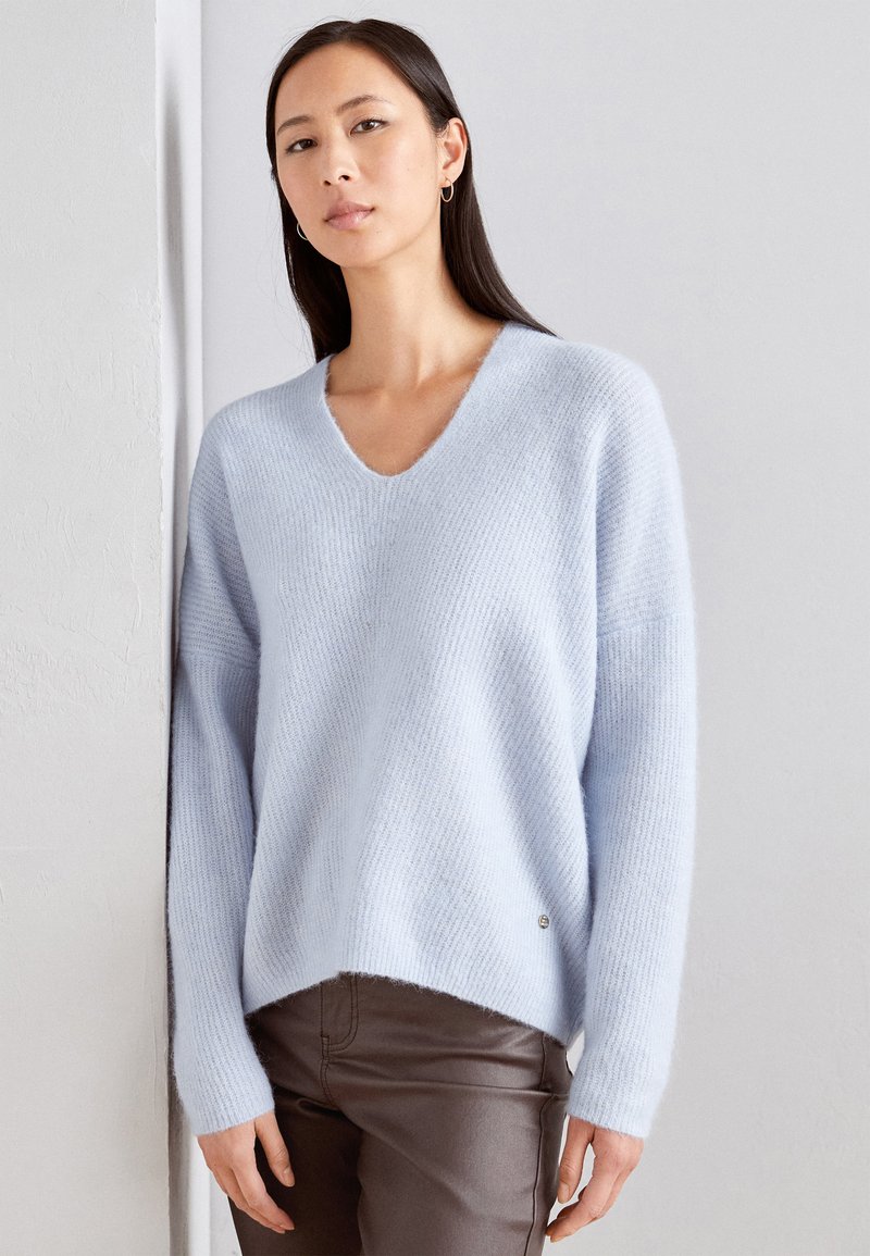 Hellblau, weicher V-Ausschnitt-Pullover mit lockerer Passform, gerippter Textur und asymmetrischem Saum, mit einem kleinen Logodetail an der Seite.