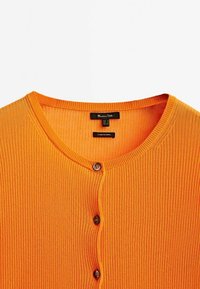 Oranger gerippter Cardigan mit rundem Ausschnitt, fünf braunen Knöpfen auf der Vorderseite und einem Stoffetikett in der Nähe des Halsausschnitts.