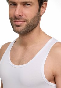 Top in cotone bianco senza maniche con spalline larghe, texture liscia e scollatura a girocollo. I dettagli importanti includono una silhouette aderente e cuciture.