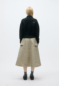 Camisola oversized preta com gola alta, combinada com uma saia acolchoada bege até ao joelho, com grandes bolsos e tecido texturizado.