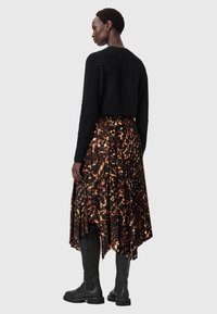 Mustat lyhyet neuleet, taittuneet hameet kiiltävällä ruskealla ja oranssilla kuviolla, yhdistettynä polven yli ulottuviin mustiin nahkasaappaisiin.