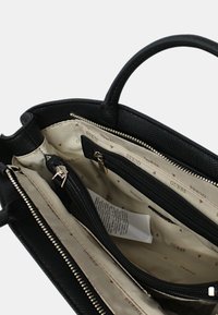 Borsa nera con interno in tessuto beige che presenta numerosi scomparti con zip e una piccola tasca, marchiata con i loghi Guess.