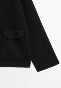 Schwarzer Strickpullover mit einer einzigen Vordertasche, klaren Linien und einer weichen Struktur. Die Ärmel haben einen geraden Schnitt.