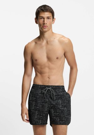 Zwarte zwemboxers met een gestructureerd patroon, voorzien van "HUGO"-branding, een elastische tailleband en een trekkoord voor een verstelbare pasvorm.