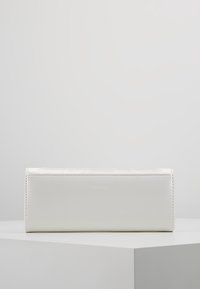Sac rectangulaire blanc avec un design texturé et des détails de couture. Présente un logo subtil à l'avant. Matériau synthétique lisse.
