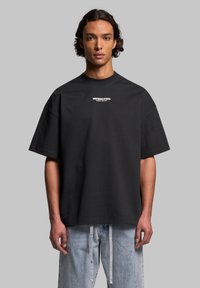 Black oversized t-shirt made of cotton with short sleeves and a crew neck, featuring white printed branding on the chest.