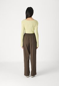 Lys gul ribbet langermet topp kombinert med brune vide bukser, med elastisk midje, sett fra baksiden, glatt tekstur.