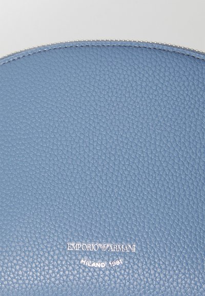 Piele texturată de culoare albastru deschis, formă rotundă, cu logo-ul embosat "EMPORIO ARMANI MILANO 1981" în argintiu la bază.