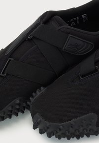 Baskets noires Puma en tissu mesh, avec des sangles réglables et des semelles texturées avec des crampons en caoutchouc proéminents pour l’adhérence.