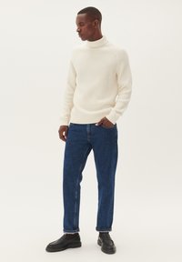 Kreminė dryžuota golfas ir mėlynos džinsinės kelnės. Aprangą papildo juodi mokasīnai, o siluetas yra laisvas.