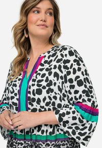 Schwarz-weiße Tierdruckbluse mit V-Ausschnitt, bunten vertikalen Streifen und Glockenärmeln in Türkis, Lila und Pink.