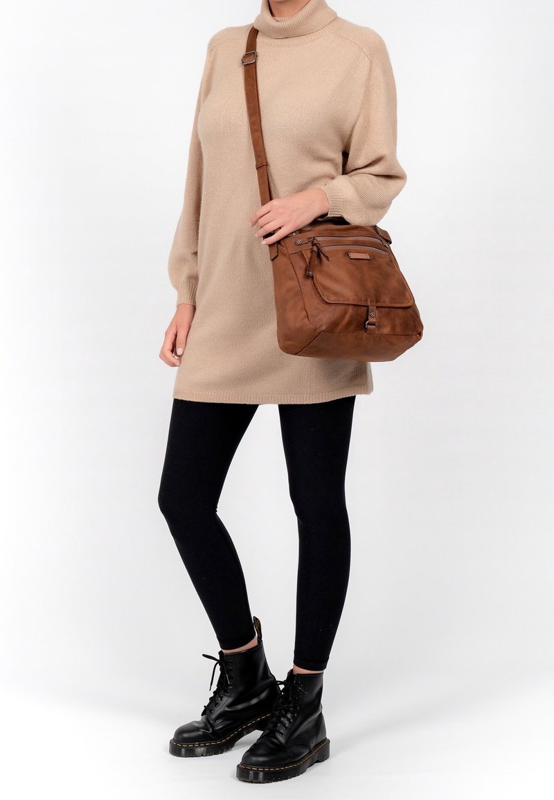 Brun läderaxelväska med flera dragkedjefickor, slät textur och robust rem. Bärs med en beige tröja och svarta leggings.