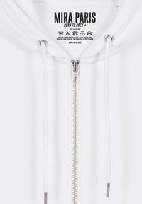 Hoodie bianco in cotone con zip frontale, cordini e etichetta con logo che dice "MIRA PARIS BORN TO ROCK." Presenta dettagli metallici sulla zip.