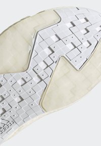 Semelle de sneaker blanche affichant des motifs texturés, comprenant des carrés surélevés et un design découpé en diagonale, avec un bord lisse, blanc cassé.