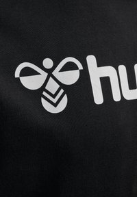 Tessuto nero con un grande logo bianco di un design di ape sopra la parola "hub". Il logo presenta dettagli distintivi delle ali e delle strisce.