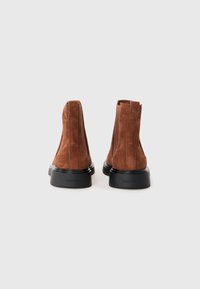 Botoșei din piele de căprioară maro, cu talpă din cauciuc negru, având un design minimalist și panouri elastice ascunse pe laterale.