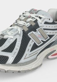 Γκρι, άσπρο και ροζ αθλητικό παπούτσι New Balance με πάνω μέρος από δίχτυ, επενδεδυμένο κολάρο και ορατή απορρόφηση κραδασμών στη σόλα.