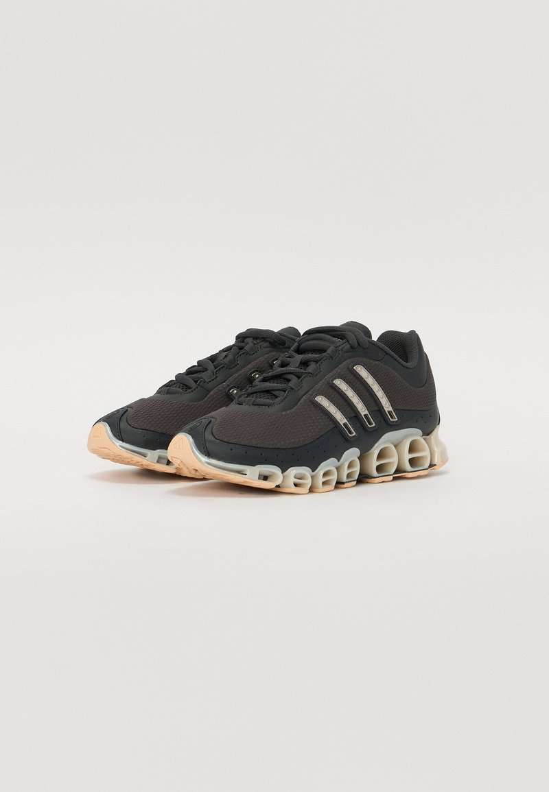 Zapatillas deportivas negras con una parte superior de tejido texturizado, tres franjas metálicas y una distintiva suela acolchada en beige y negro.