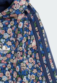 Bloemrijke hoodie met een marineblauwe basis, voorzien van kleurvolle bloemenpatronen, een gestructureerde stof en donkerblauwe gestreepte accenten aan de zijkanten.