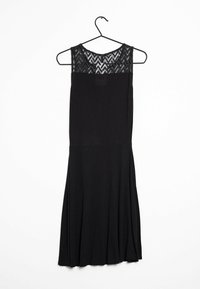 Schwarzes Kleid an einem Kleiderbügel mit einem durchsichtigen, zigzag-musternden Spitzen-Oberteil und tailliertem Schnitt, das in einen sanft ausgestellten Rock übergeht.