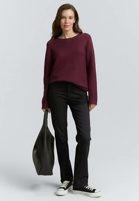 Bordowy sweter z długim rękawem o fakturze, czarne dopasowane spodnie i czarne tenisówki. Modelka niesie dużą ciemnozieloną torbę typu tote.