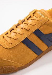 Sneakers in suede arancione-giallo con strisce blu navy. Presentano una superficie texture, lacci piatti e una suola in gomma.