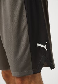 Pantalones cortos deportivos Puma en gris y negro, con una textura de malla, paneles laterales en contraste y un logo blanco en la parte inferior de la pierna.