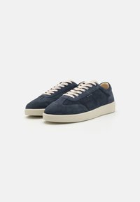 Suede sneakers in navy blue with a white rubber sole. Features cream laces and subtle perforations on the side for ventilation.