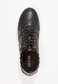Sneaker nera Guess con motivo in rilievo del logo, lacci neri e emblema laterale in tonalità argento su sfondo bianco.