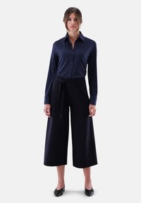 Navy button-up shirt with long sleeves paired with high-waisted wide-leg dark pants, featuring a tied belt and smooth texture.