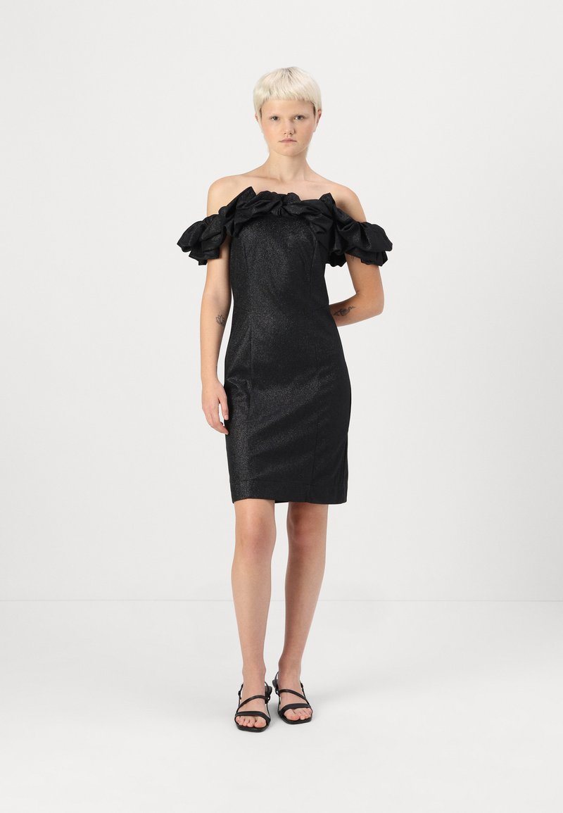 Μαύρο φόρεμα με ανοιχτούς ώμους και βολάν μανίκια, φτιαγμένο από γυαλιστερό ύφασμα. Εφαρμοστό σιλουέτα, με μήκος μέχρι το γόνατο, σε συνδυασμό με μαύρες σαγιονάρες.