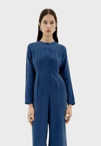 Blauwe linnen jumpsuit met lange mouwen, knoopsluiting bij de halslijn, geplooid ontwerp op de borst en een comfortabele pasvorm. Stijlvolle textuur en minimale details.