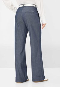 Brede broekspijpen in donker denim met een gladde textuur. Beschikt over een witte tailleband en achterzakken. De zoom is licht omgeslagen.