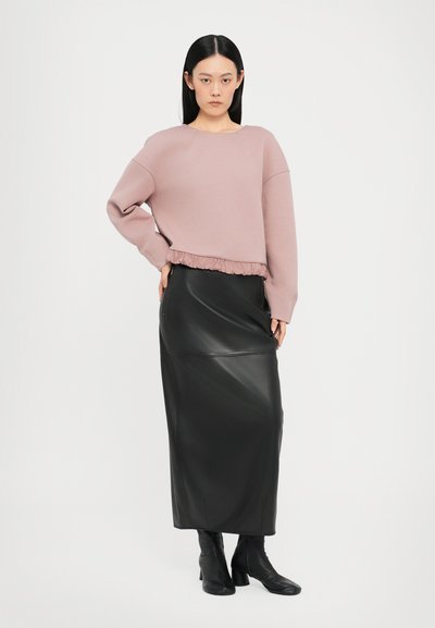 Himmelblaues, kurzes Sweatshirt mit gerüschtem Saum, kombiniert mit einem schwarzen Leder-Maxi-Rock. Das Model trägt schwarze Knöchelstiefel. Schlichter Hintergrund.