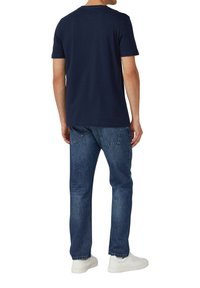 Granatowa koszulka z krótkim rękawem, wykonana z bawełny, z okrągłym dekoltem, zestawiona z niebieskimi dżinsami i białymi sneakersami.