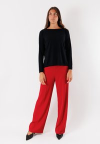 Maglietta nera a maniche lunghe con scollatura quadrata abbinata a pantaloni rossi larghi, entrambi realizzati in tessuto liscio. Scarpe nere a punta.